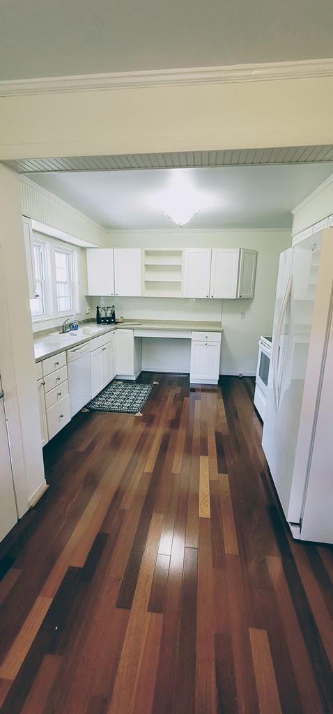 kitchen with dark wood-style floors, light countertops, white appliances, and white cabinets