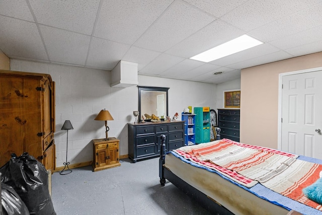 bedroom featuring a drop ceiling, concrete block wall, and finished concrete floors