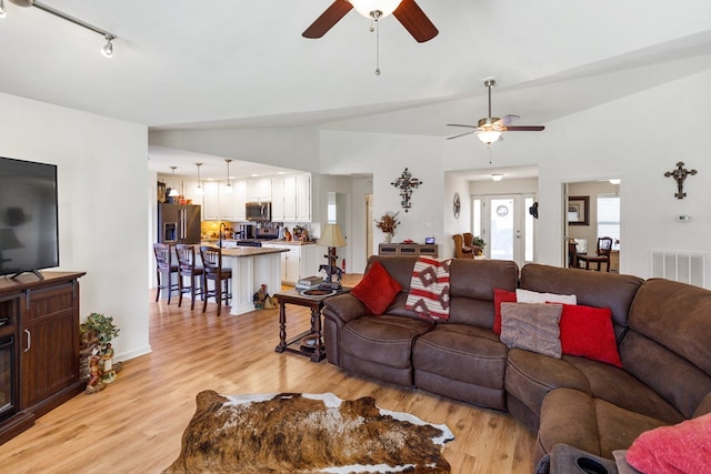 living room featuring light wood finished floors, visible vents, vaulted ceiling, and rail lighting