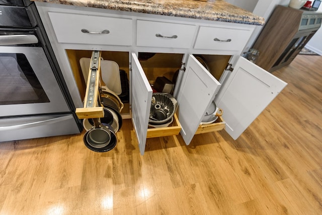 details with light wood finished floors, stainless steel range with electric stovetop, white cabinetry, and light stone countertops