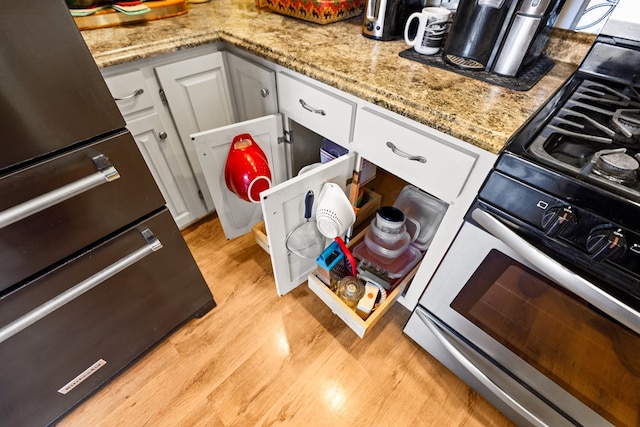 interior space featuring light wood finished floors, stainless steel range with gas cooktop, white cabinetry, and light stone counters