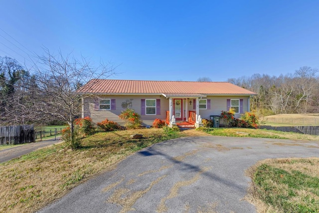 ranch-style house featuring metal roof, a front yard, fence, and driveway