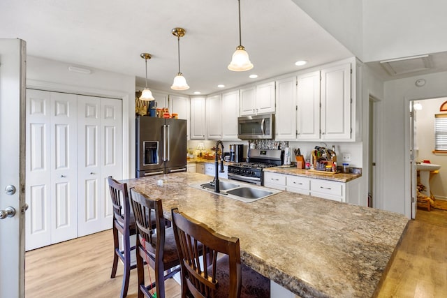 kitchen with stainless steel appliances, hanging light fixtures, light wood-style flooring, and white cabinetry