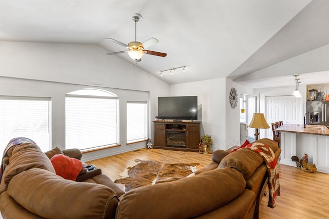 living area with lofted ceiling, light wood-style floors, a fireplace, and a ceiling fan