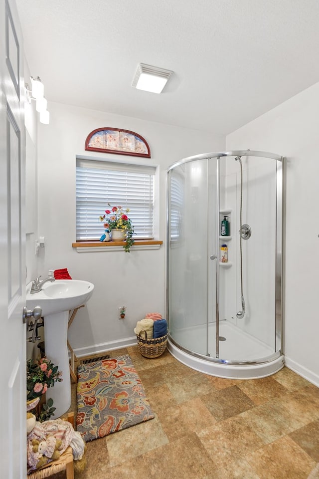 bathroom with a stall shower, a sink, stone finish floor, and baseboards