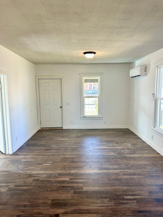 empty room with dark wood finished floors, a textured ceiling, and a wall mounted air conditioner