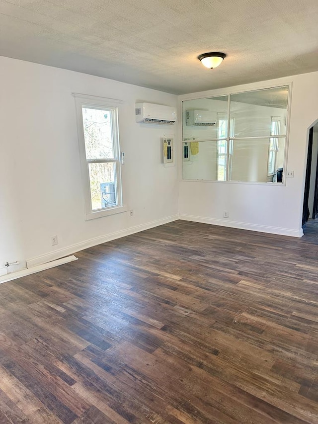 unfurnished room with a wall unit AC, dark wood-type flooring, and a textured ceiling