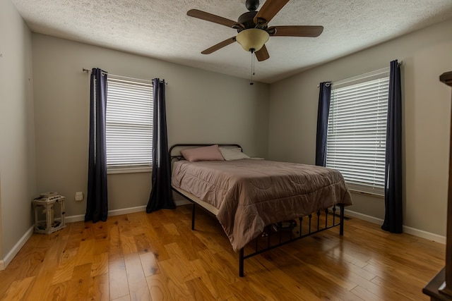 bedroom with light wood finished floors, ceiling fan, baseboards, and a textured ceiling