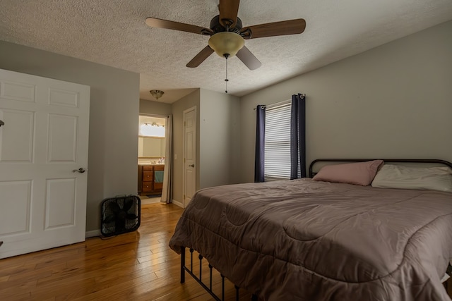 bedroom featuring light wood-style flooring, ensuite bathroom, a ceiling fan, a textured ceiling, and baseboards