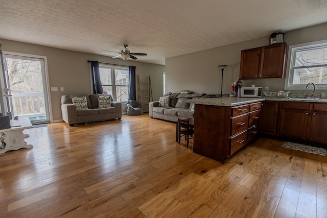 kitchen with light wood-style flooring, open floor plan, a peninsula, a textured ceiling, and a sink