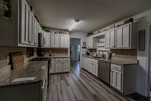 kitchen with white cabinets, dark stone countertops, light wood-type flooring, black appliances, and a sink