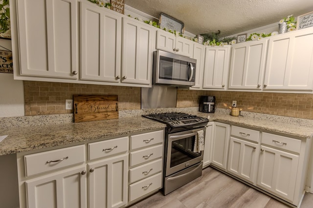 kitchen with a textured ceiling, light stone counters, white cabinets, appliances with stainless steel finishes, and decorative backsplash