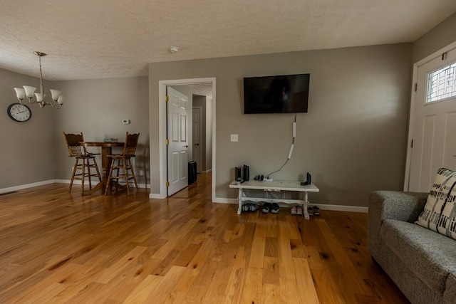 living area featuring a textured ceiling, a notable chandelier, wood finished floors, and baseboards