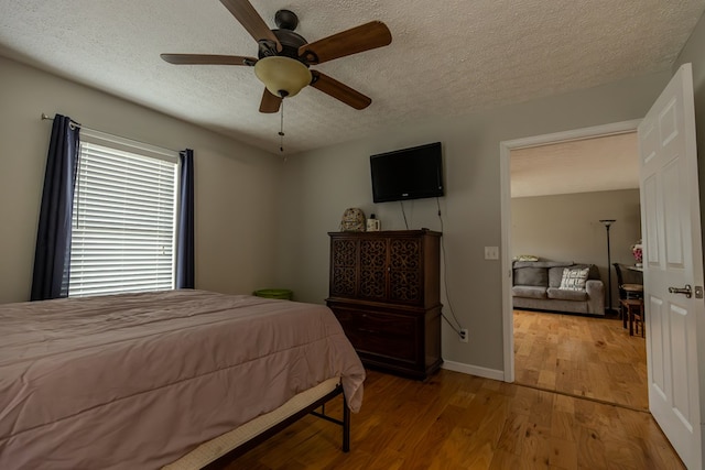 bedroom with a textured ceiling, baseboards, light wood-style flooring, and a ceiling fan