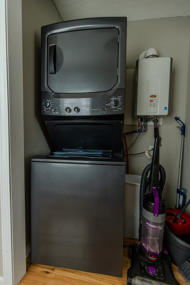 washroom with light wood-type flooring, stacked washing maching and dryer, laundry area, and tankless water heater