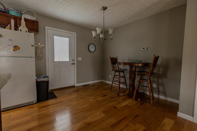 dining room featuring visible vents, baseboards, wood finished floors, a textured ceiling, and a chandelier