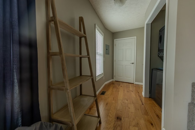 doorway with a textured ceiling, visible vents, baseboards, stacked washing maching and dryer, and light wood finished floors