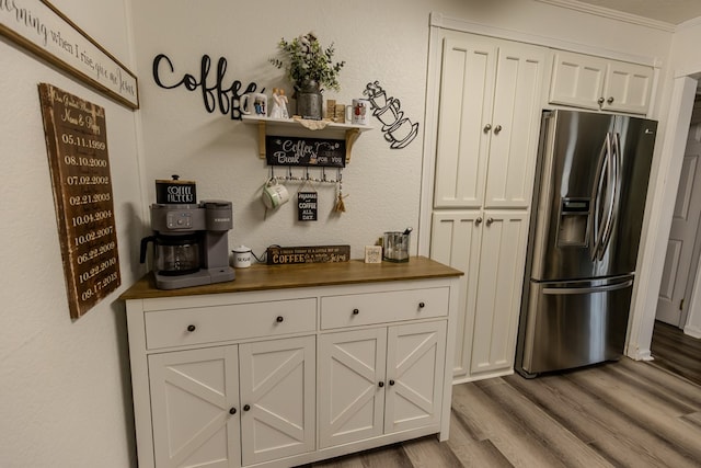 kitchen featuring stainless steel fridge, white cabinetry, light wood-style flooring, and a textured wall