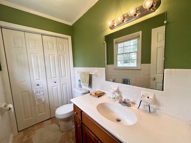 bathroom featuring toilet, vanity, tile walls, ornamental molding, and a closet