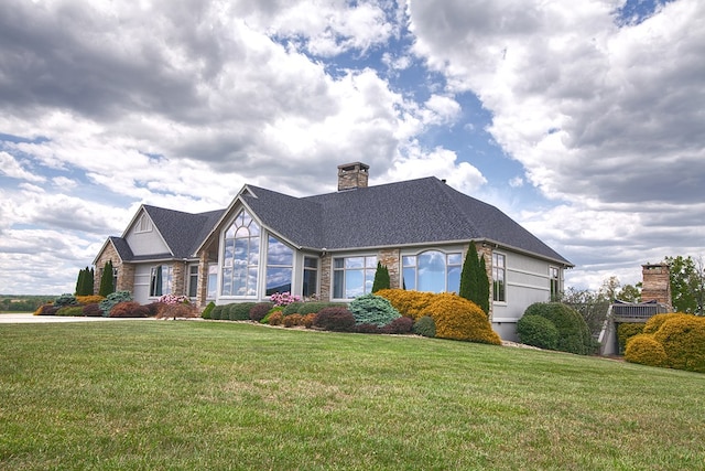 view of front of house with a shingled roof, a front yard, brick siding, and a chimney