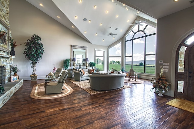 living area featuring arched walkways, dark wood finished floors, ceiling fan, a fireplace, and high vaulted ceiling