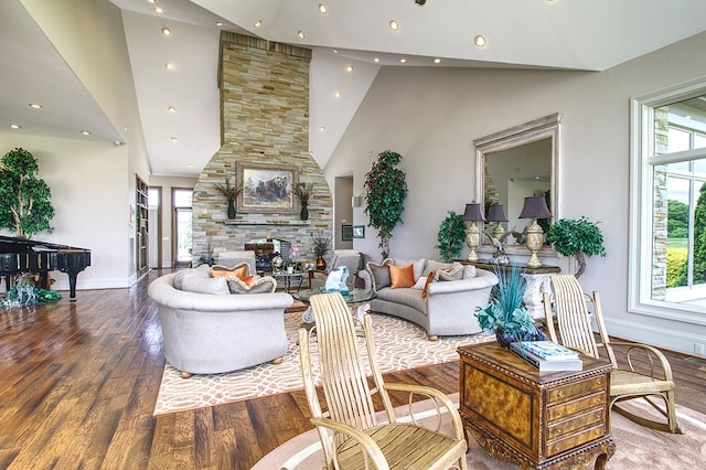 living area featuring recessed lighting, a stone fireplace, wood finished floors, high vaulted ceiling, and baseboards