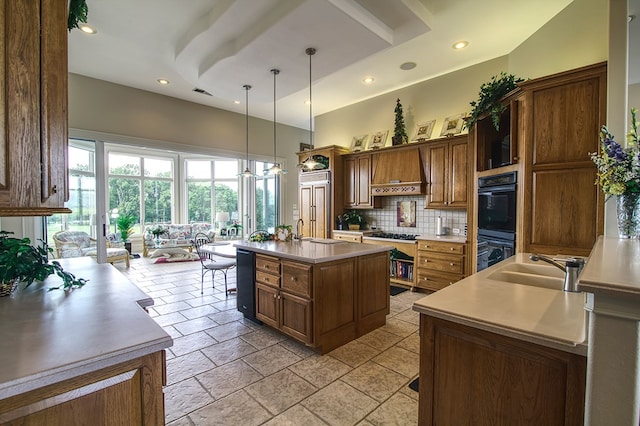 kitchen with dobule oven black, an island with sink, decorative light fixtures, light countertops, and a sink