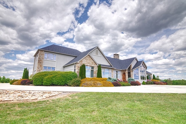 traditional-style home with stone siding, a chimney, a front lawn, and stucco siding