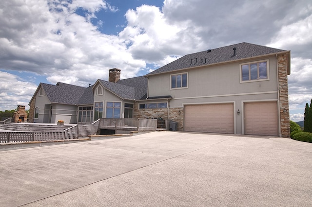 back of property featuring stone siding, concrete driveway, an attached garage, and stucco siding