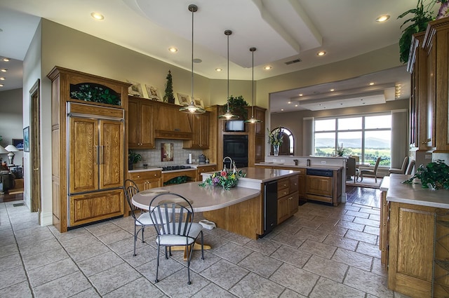 kitchen with paneled built in refrigerator, light countertops, brown cabinets, an island with sink, and pendant lighting