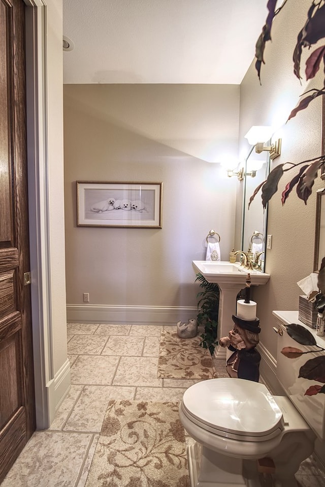 half bath featuring baseboards, stone tile floors, a sink, and toilet