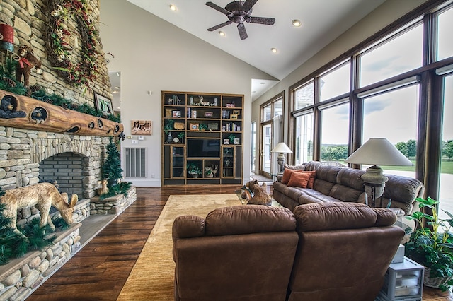 living area featuring ceiling fan, high vaulted ceiling, a stone fireplace, dark wood-type flooring, and visible vents