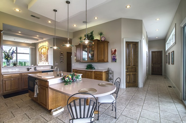 kitchen with a sink, visible vents, light countertops, brown cabinets, and glass insert cabinets