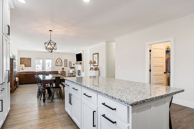 kitchen with light stone counters, wood finished floors, ornamental molding, open floor plan, and a center island