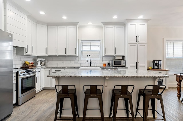 kitchen featuring a wealth of natural light, a sink, a kitchen breakfast bar, appliances with stainless steel finishes, and crown molding