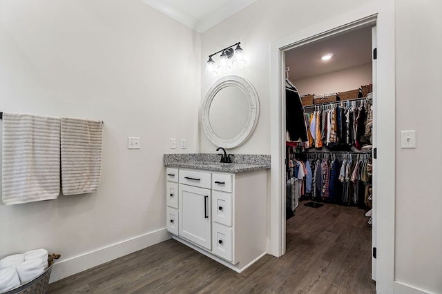 bathroom featuring ornamental molding, wood finished floors, vanity, baseboards, and a spacious closet