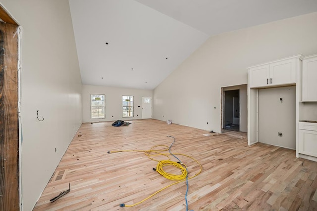 unfurnished living room with high vaulted ceiling, light wood finished floors, and visible vents