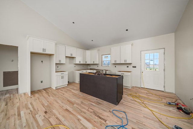 kitchen with high vaulted ceiling, a center island, white cabinetry, and light wood-style floors