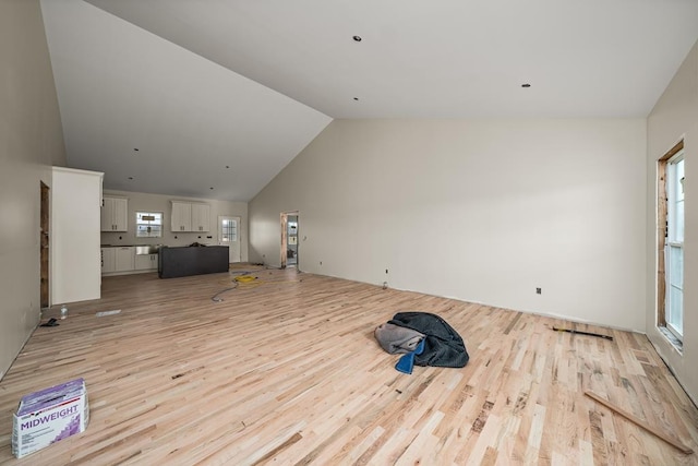 unfurnished living room with high vaulted ceiling, a healthy amount of sunlight, and light wood-style flooring