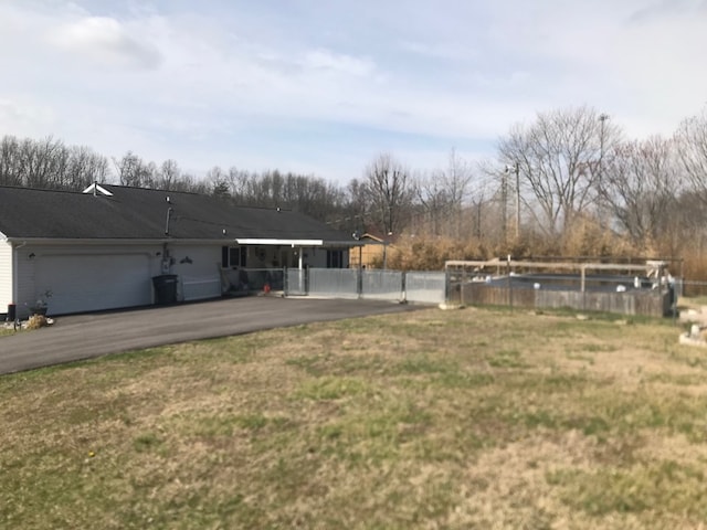 view of yard with aphalt driveway, an attached garage, and fence