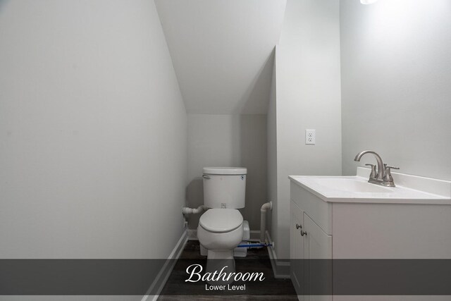 half bathroom featuring lofted ceiling, toilet, wood finished floors, vanity, and baseboards