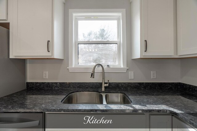 kitchen featuring dark stone countertops, a sink, and white cabinetry