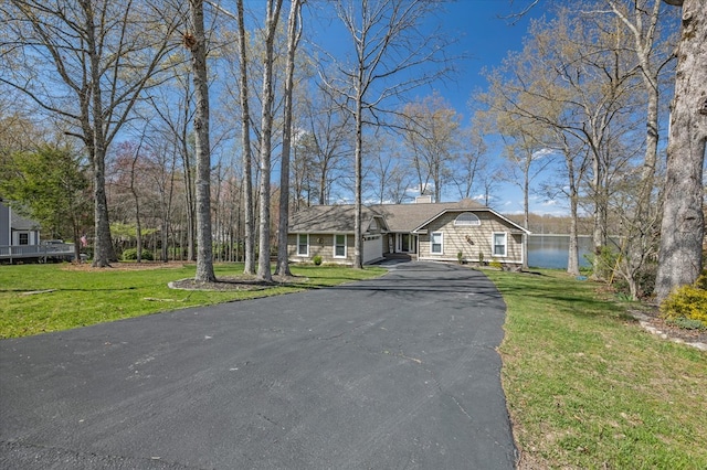 view of front of house featuring a water view, a chimney, aphalt driveway, and a front yard