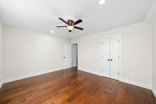 unfurnished bedroom featuring dark wood-style floors, a closet, baseboards, and a ceiling fan