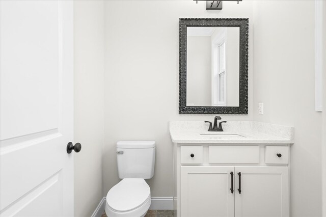 half bathroom with baseboards, vanity, and toilet