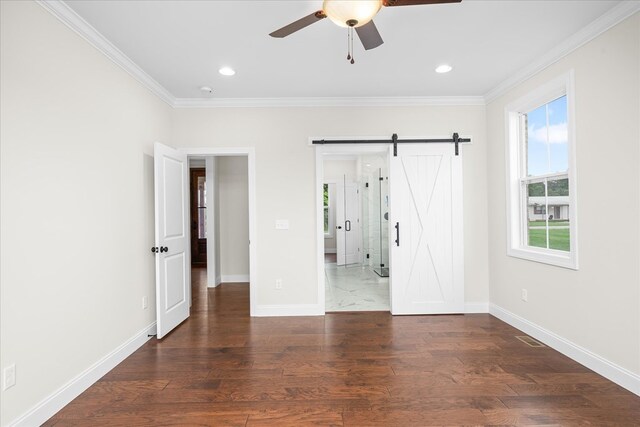 unfurnished bedroom with dark wood-type flooring, crown molding, baseboards, and a barn door