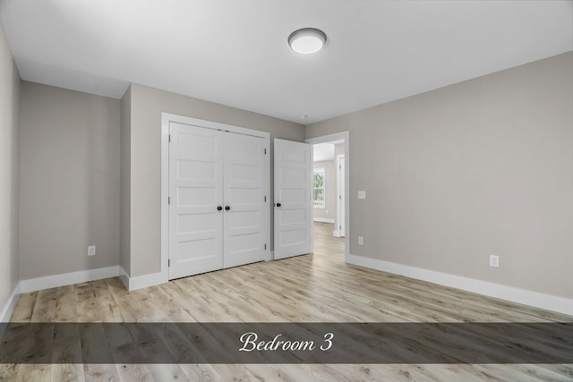 unfurnished bedroom featuring light wood-style flooring, baseboards, and a closet