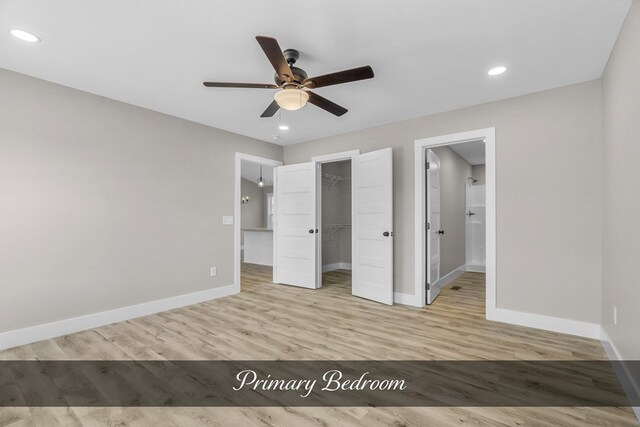 unfurnished bedroom with baseboards, a walk in closet, and light wood-style floors