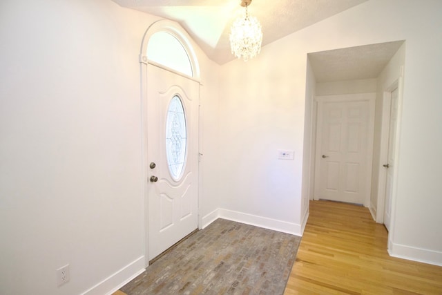 entrance foyer featuring lofted ceiling, baseboards, a chandelier, and wood finished floors