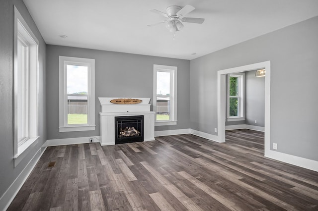 unfurnished living room with dark wood-style floors, ceiling fan, a fireplace, and baseboards